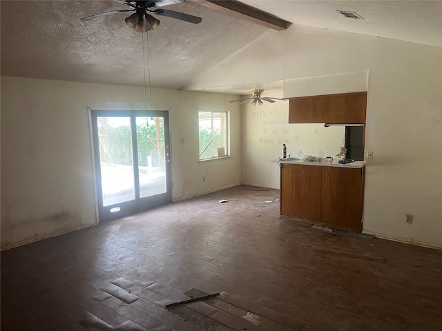 unfurnished living room featuring ceiling fan, vaulted ceiling with beams, a textured ceiling, and dark hardwood / wood-style floors