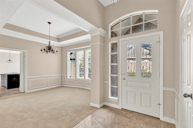 carpeted foyer featuring crown molding, a chandelier, decorative columns, and a tray ceiling