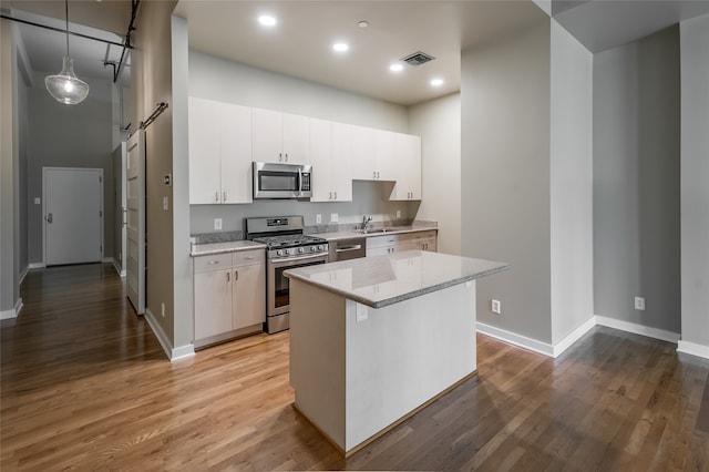 kitchen with white cabinets, hanging light fixtures, a barn door, appliances with stainless steel finishes, and a kitchen island