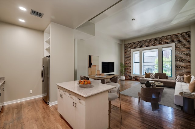 kitchen with stainless steel fridge, brick wall, a kitchen island, light hardwood / wood-style floors, and white cabinetry