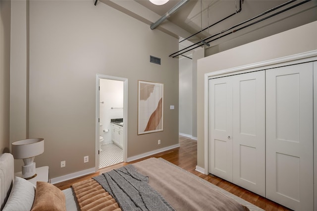 bedroom featuring light wood-type flooring, a towering ceiling, ensuite bathroom, and a closet