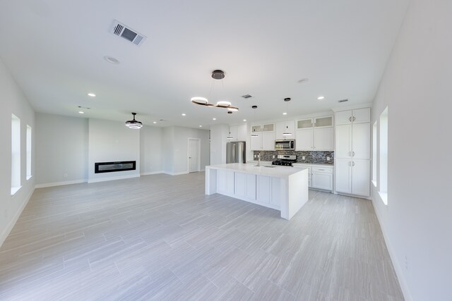 kitchen featuring pendant lighting, an island with sink, tasteful backsplash, white cabinetry, and stainless steel appliances