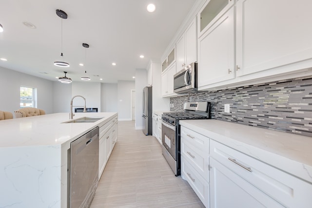 kitchen featuring white cabinets, decorative light fixtures, a center island with sink, backsplash, and appliances with stainless steel finishes