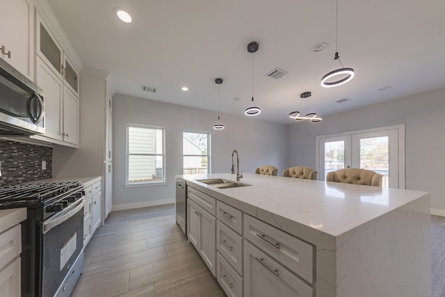 kitchen featuring hanging light fixtures, sink, a center island with sink, white cabinetry, and appliances with stainless steel finishes