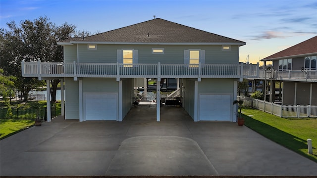 back house at dusk featuring a garage, a yard, a carport, and a balcony