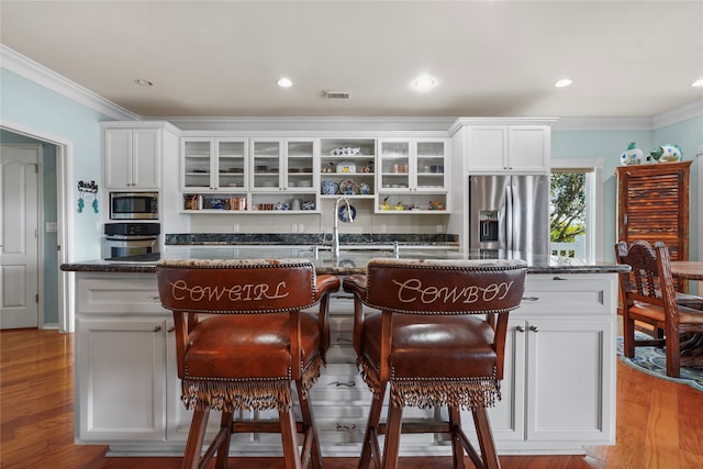 kitchen featuring white cabinets, a center island with sink, appliances with stainless steel finishes, and light hardwood / wood-style flooring