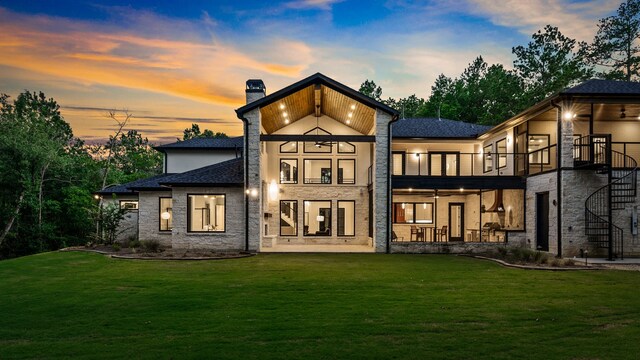 back house at dusk featuring a balcony and a lawn