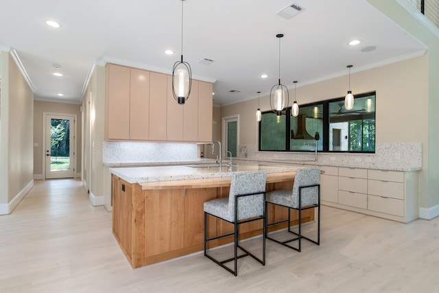 kitchen featuring light stone counters, light hardwood / wood-style flooring, ornamental molding, light brown cabinetry, and backsplash