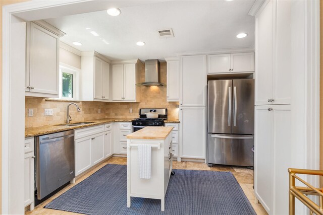 kitchen featuring sink, wall chimney exhaust hood, light stone countertops, white cabinetry, and stainless steel appliances