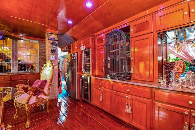 bar with wine cooler, stainless steel refrigerator, light stone countertops, and dark wood-type flooring