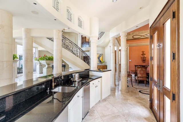 kitchen featuring white cabinets, sink, dark stone countertops, stainless steel dishwasher, and decorative columns