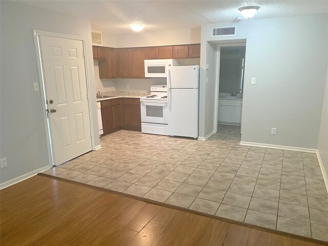 kitchen featuring a textured ceiling, light wood-type flooring, sink, and white appliances