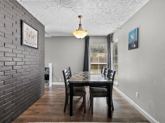 dining space featuring dark hardwood / wood-style flooring, a textured ceiling, and brick wall