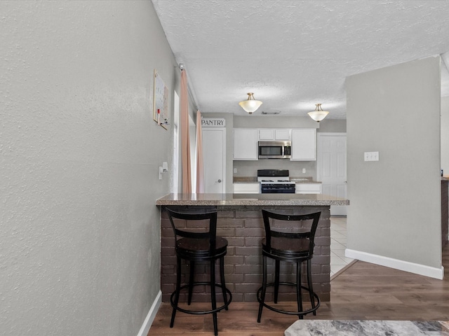 kitchen featuring kitchen peninsula, a breakfast bar, white cabinets, and white range with gas stovetop