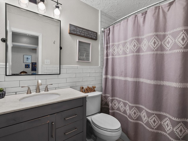 bathroom with vanity, toilet, a textured ceiling, and tile walls