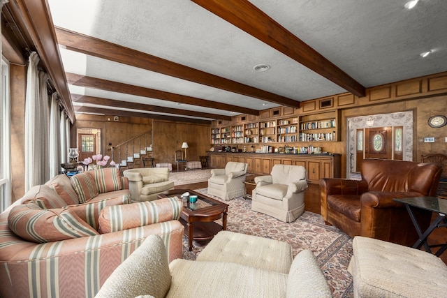 living room featuring beamed ceiling, a textured ceiling, and wooden walls