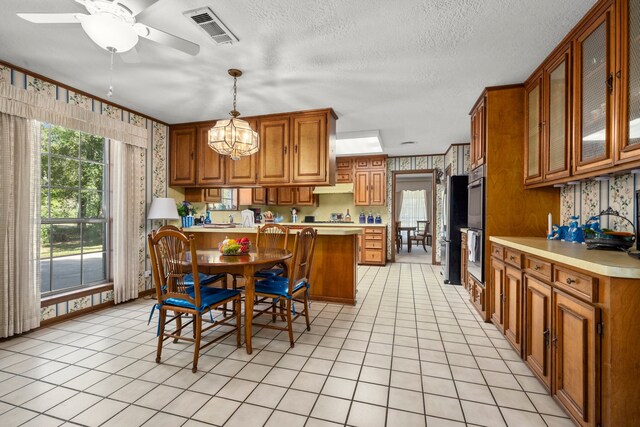 kitchen with light tile patterned floors, kitchen peninsula, a textured ceiling, decorative light fixtures, and ceiling fan with notable chandelier