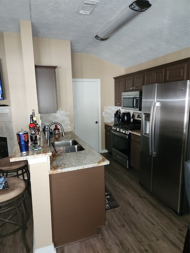 kitchen featuring sink, kitchen peninsula, a textured ceiling, appliances with stainless steel finishes, and a kitchen bar