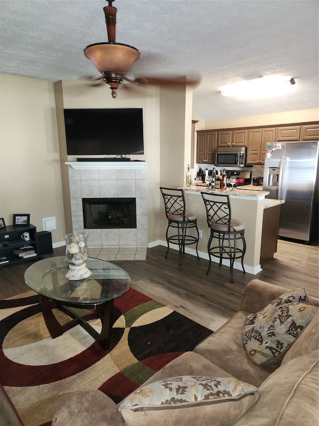 living room featuring ceiling fan, light hardwood / wood-style floors, a textured ceiling, and a tiled fireplace