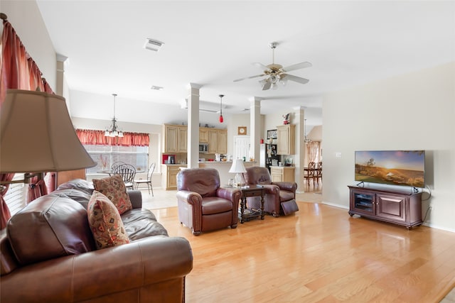 living room with ceiling fan with notable chandelier, light wood-type flooring, ornate columns, and a healthy amount of sunlight