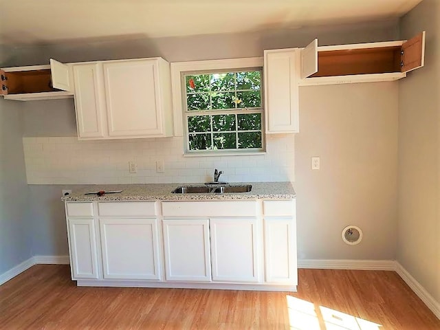 kitchen with light stone counters, white cabinets, light wood-type flooring, and sink