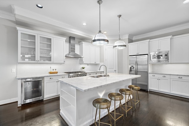 kitchen featuring stainless steel appliances, white cabinets, beverage cooler, wall chimney range hood, and a center island with sink