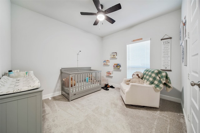 bedroom with a crib, light carpet, and ceiling fan