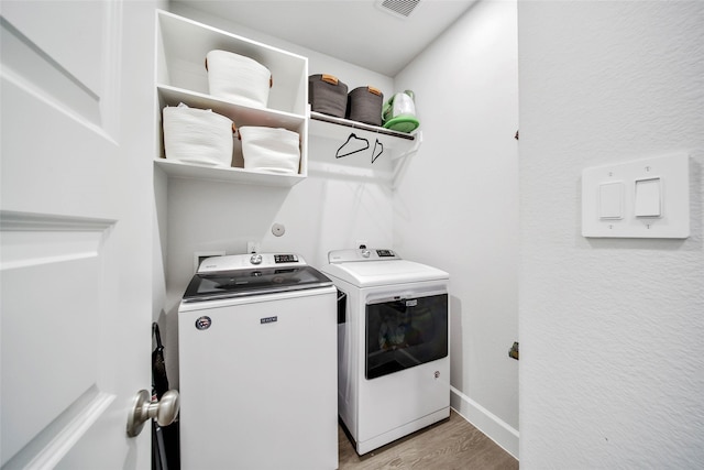 laundry area with washing machine and clothes dryer and light hardwood / wood-style floors