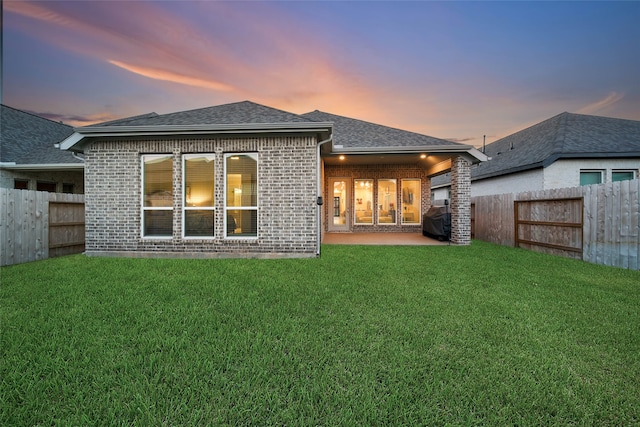 back house at dusk with a lawn and a patio area