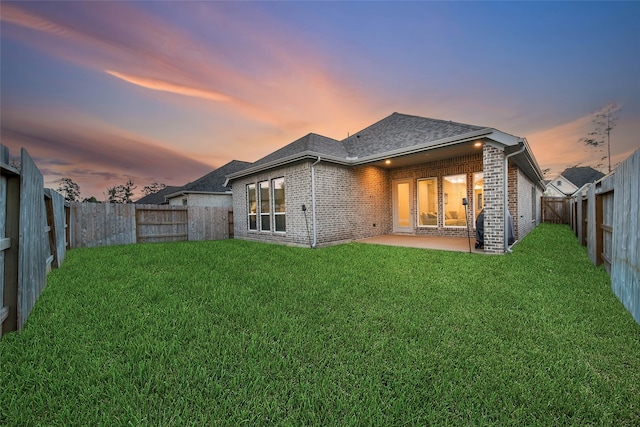 back house at dusk with a yard and a patio area