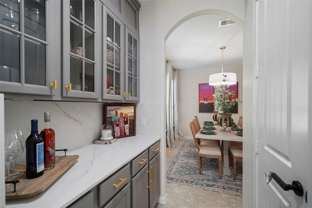 bar with light stone counters, decorative light fixtures, gray cabinets, and tasteful backsplash