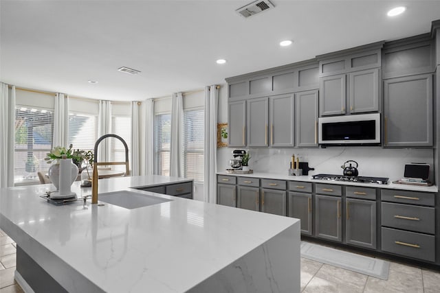 kitchen featuring a large island with sink, sink, light stone counters, and gray cabinets