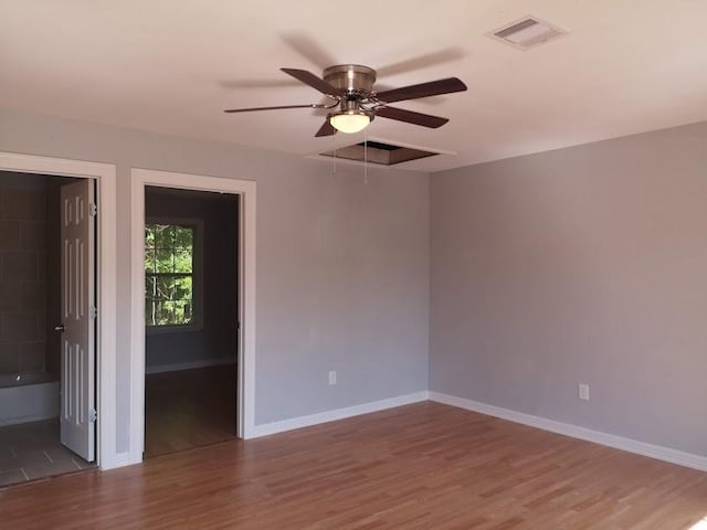 empty room with attic access, a ceiling fan, baseboards, wood finished floors, and visible vents