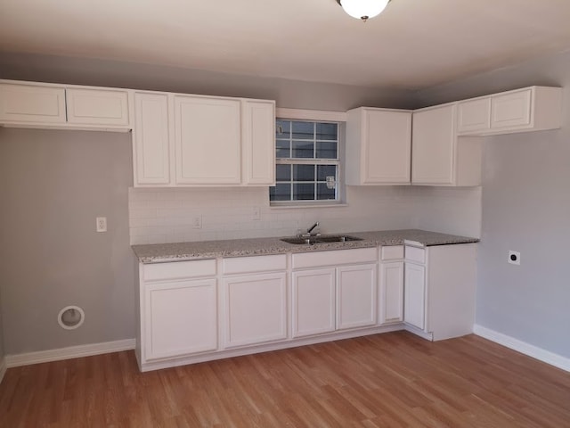 kitchen featuring backsplash, white cabinetry, light stone countertops, light hardwood / wood-style floors, and sink