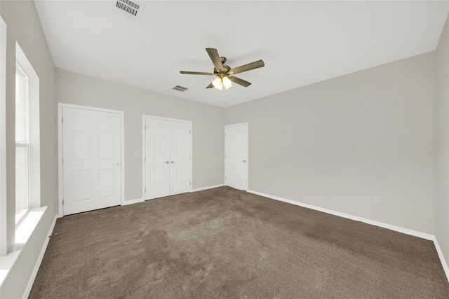 unfurnished bedroom featuring ceiling fan, multiple closets, and dark carpet