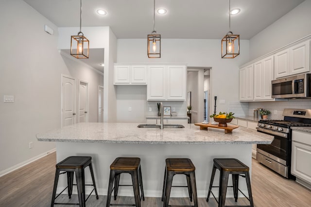 kitchen featuring white cabinets, sink, a kitchen island with sink, decorative light fixtures, and appliances with stainless steel finishes