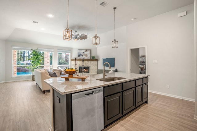 kitchen featuring light stone counters, an island with sink, sink, dishwasher, and a fireplace