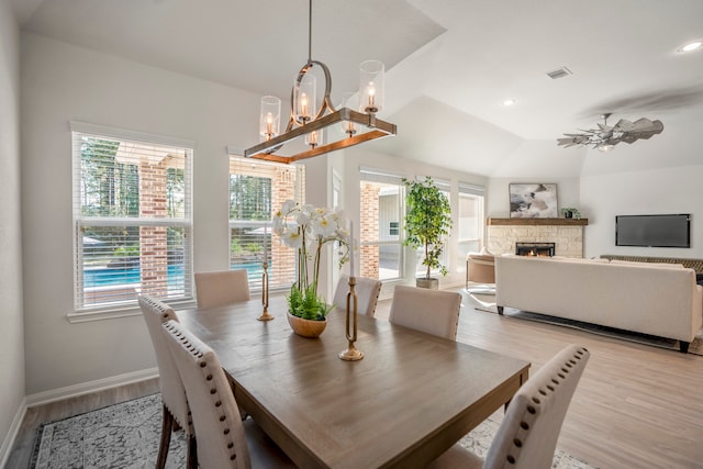 dining space featuring ceiling fan with notable chandelier, a fireplace, lofted ceiling, and light hardwood / wood-style flooring