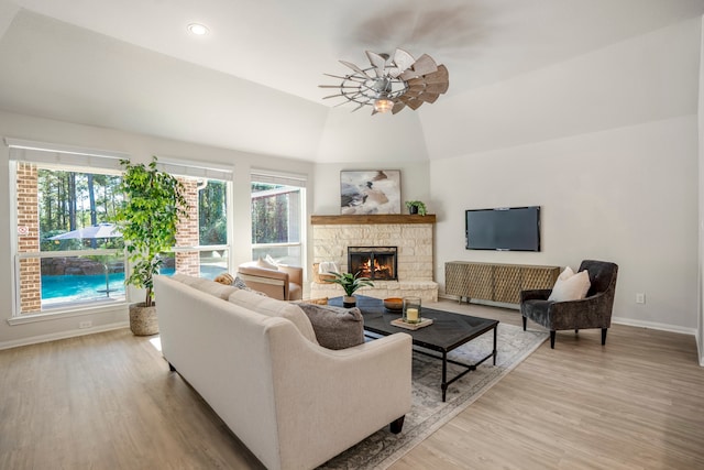 living room featuring lofted ceiling, ceiling fan, a stone fireplace, and light hardwood / wood-style flooring