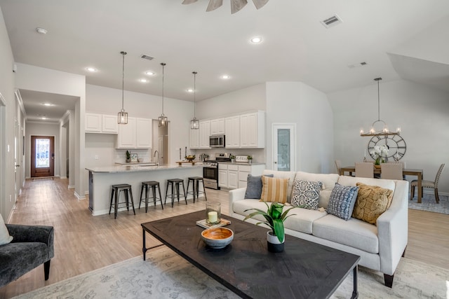 living room with light wood-type flooring, vaulted ceiling, and an inviting chandelier