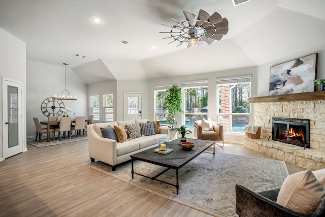 living room with ceiling fan with notable chandelier, light hardwood / wood-style floors, a fireplace, and vaulted ceiling