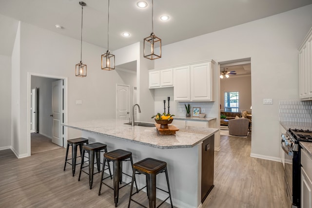 kitchen with white cabinets, hanging light fixtures, sink, a kitchen island with sink, and gas stove