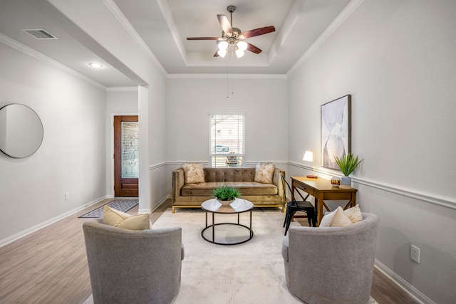 living room with light hardwood / wood-style floors, a tray ceiling, ornamental molding, and ceiling fan