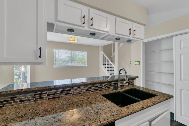 kitchen with white cabinetry, backsplash, dark stone countertops, and sink