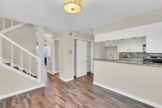 kitchen with light stone countertops, white cabinetry, dark hardwood / wood-style flooring, appliances with stainless steel finishes, and tasteful backsplash