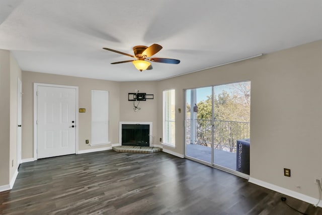 unfurnished living room with ceiling fan, a brick fireplace, plenty of natural light, and dark hardwood / wood-style floors