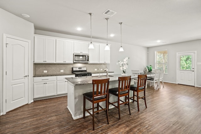 kitchen featuring stainless steel appliances, an island with sink, white cabinets, and dark hardwood / wood-style flooring