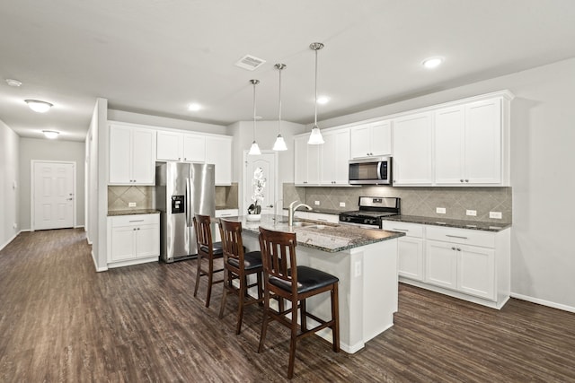 kitchen featuring pendant lighting, dark wood-type flooring, stainless steel appliances, an island with sink, and white cabinets