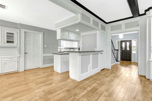 kitchen with kitchen peninsula, a textured ceiling, white cabinetry, dark stone counters, and light hardwood / wood-style floors