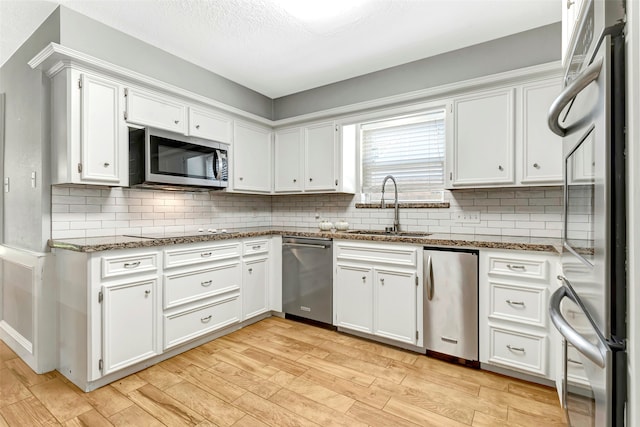 kitchen with light hardwood / wood-style floors, dark stone countertops, sink, stainless steel appliances, and white cabinets